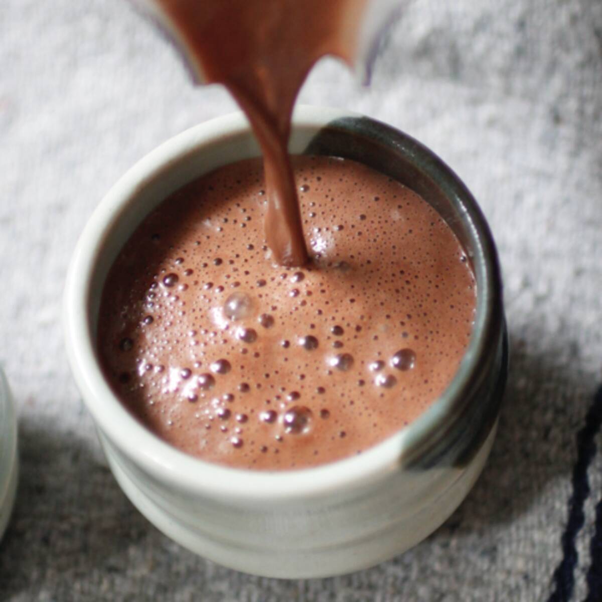 Ceremonial cacao drink being poured into a ceramic mug, showing the rich dark chocolate texture