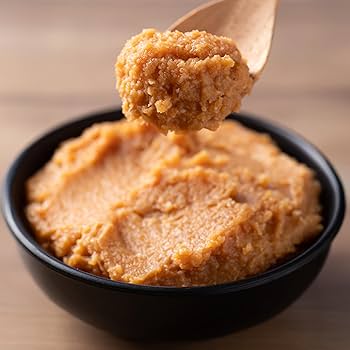 A bowl of raw chickpea miso paste on a wooden spoon
